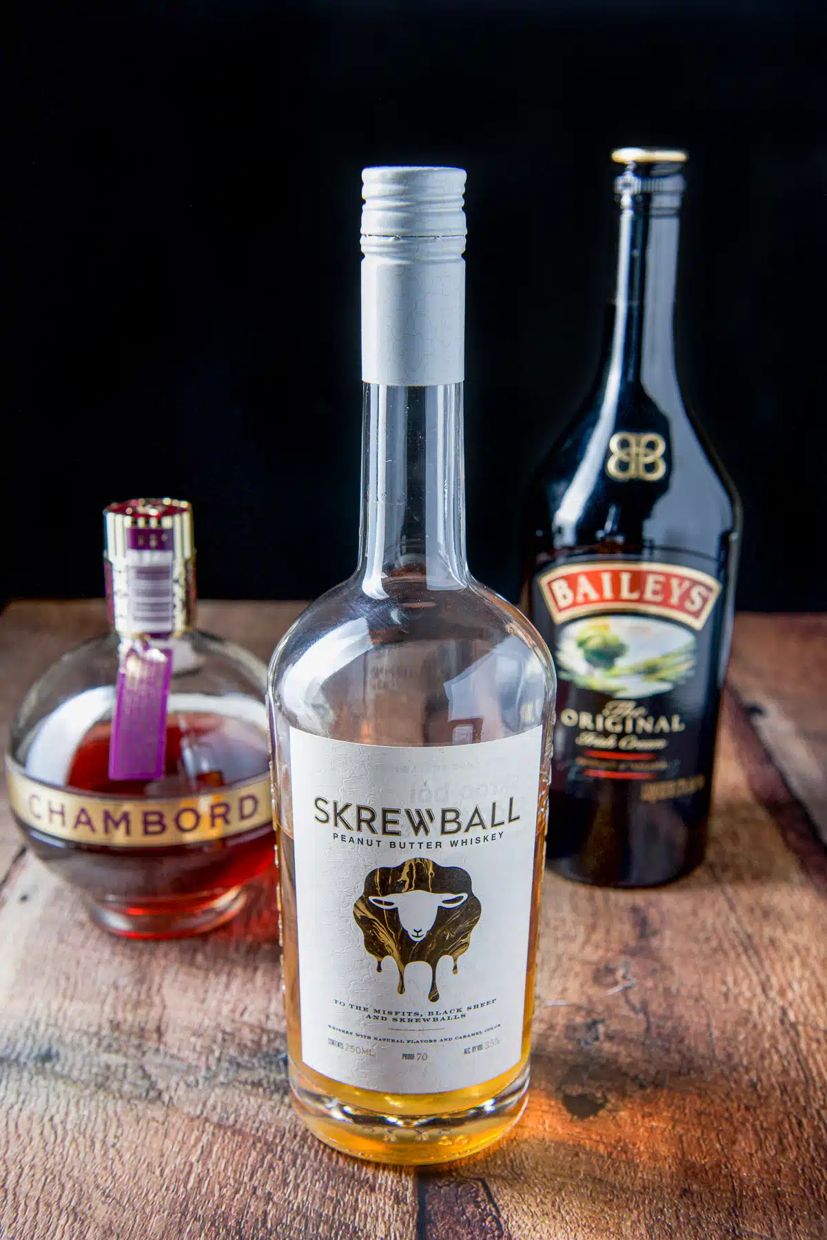 Skrewball whiskey, Chambord, and Baileys Irish cream on a wood table