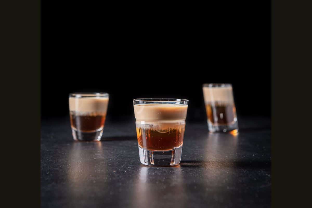 Vertical view of the beveled glass filled with the layered shot with the two glasses behind it