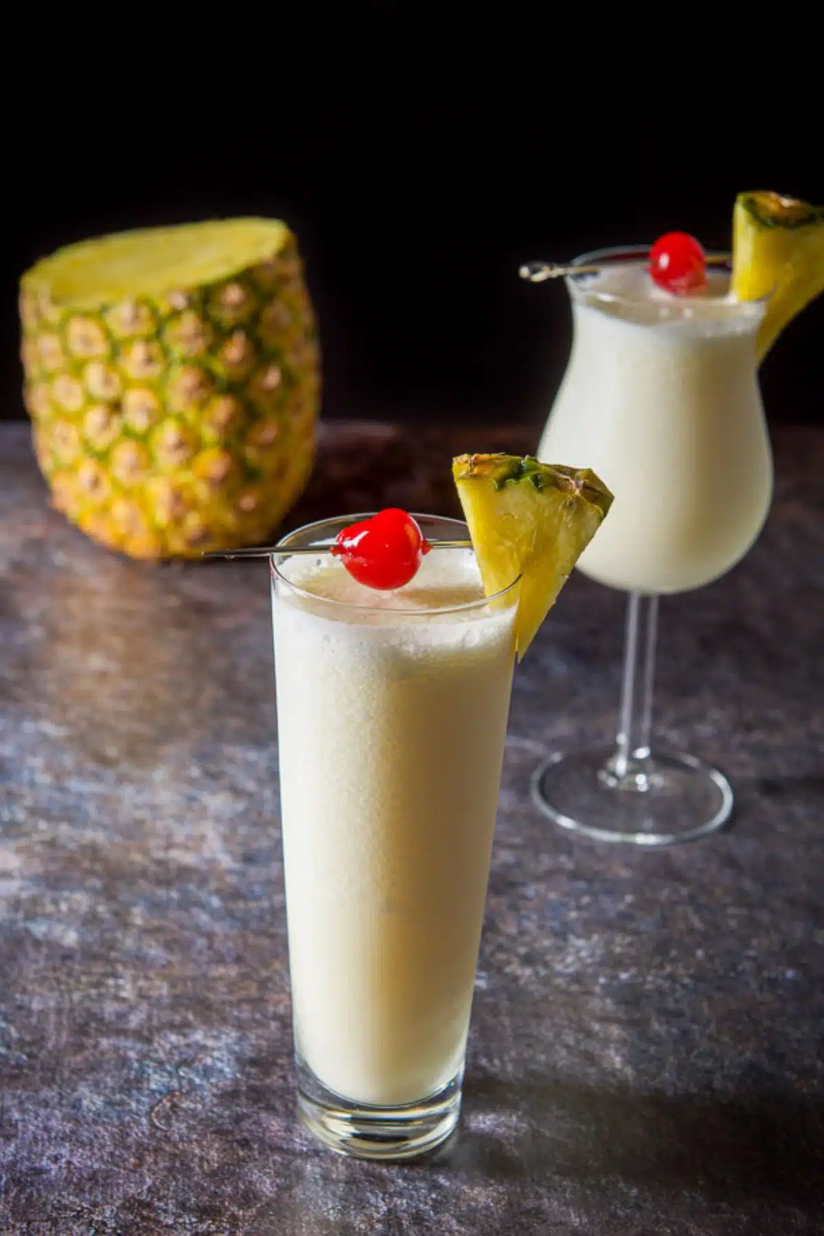 Two glasses with the pina colada with a most of a pineapple in the background