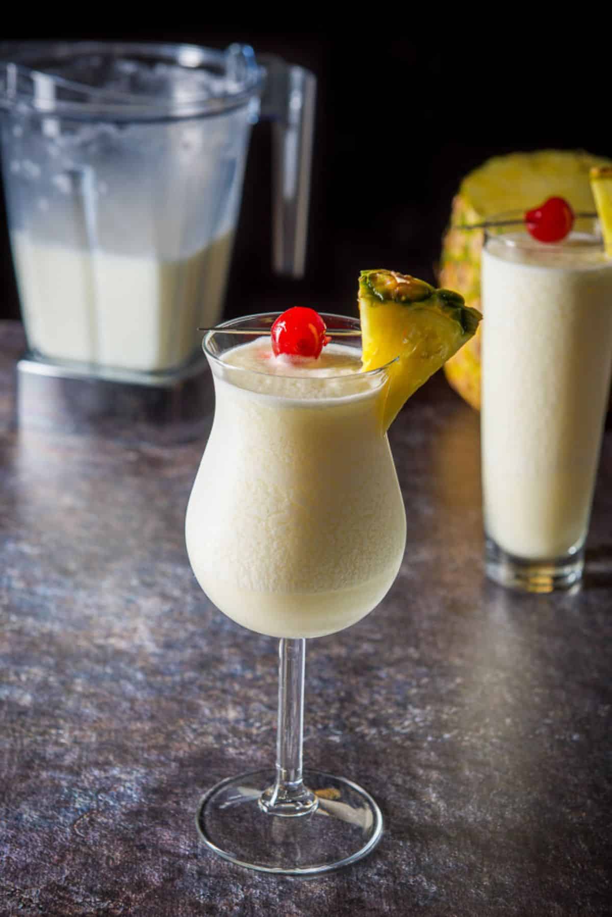 Pina colada cocktail in two glasses with more in the blender behind them