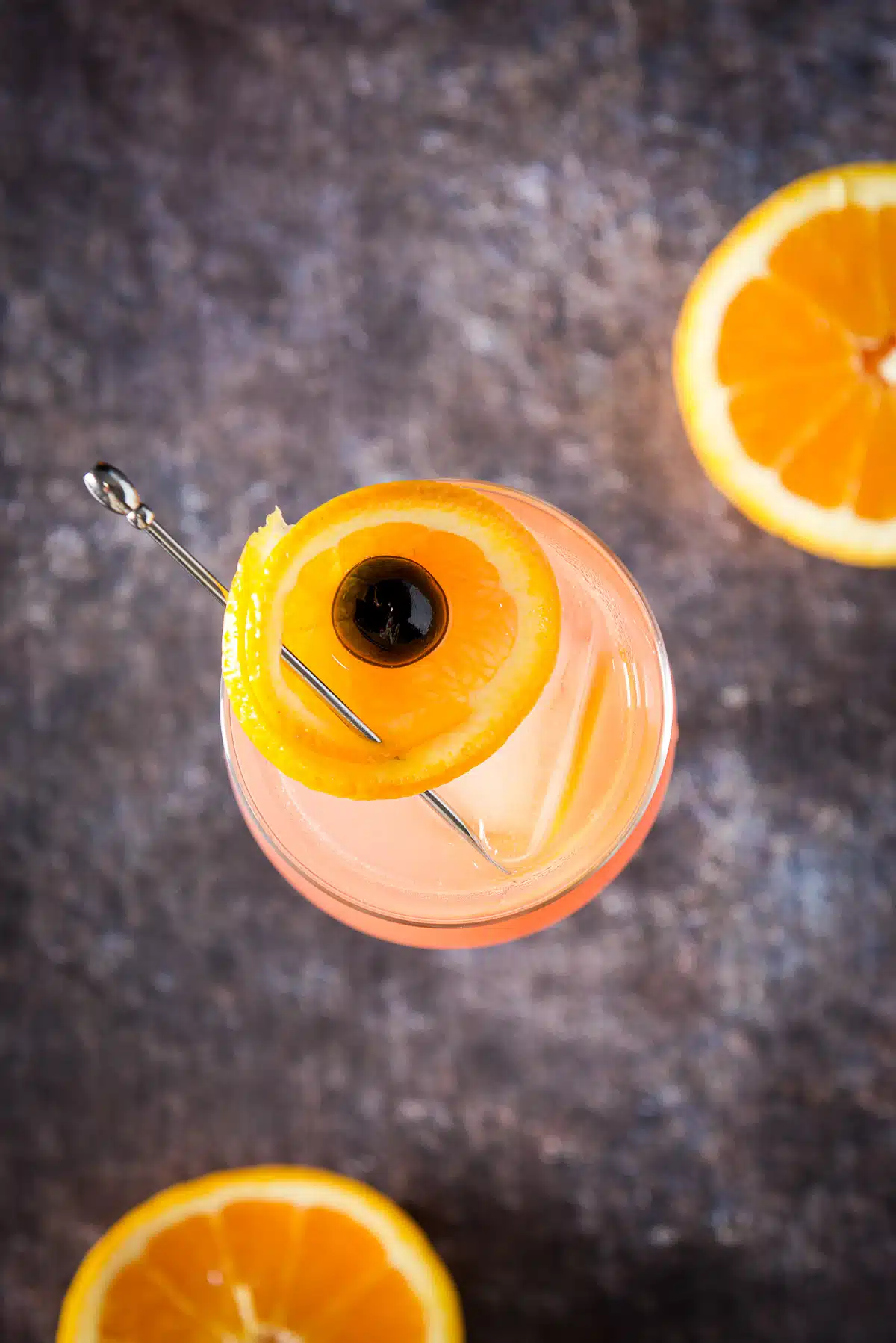 Overhead view of the cocktail with the orange cup garnish featured and the orange slices on table