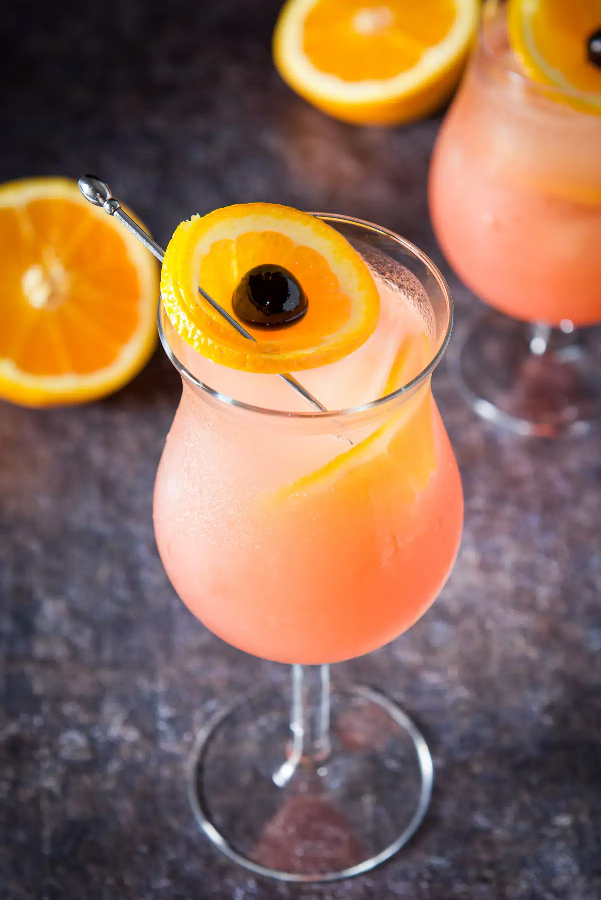 Two glasses with the orange cocktail in them with orange slices and cherries