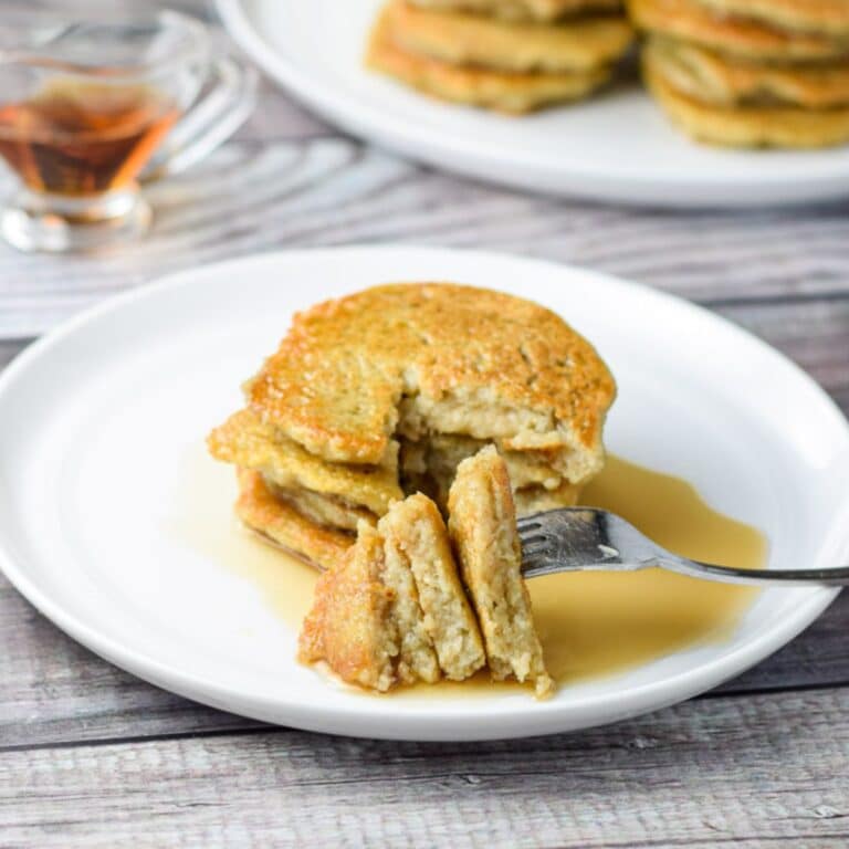 A white plate with pancakes on it with syrup, and cut in triangles on a fork on it's side
