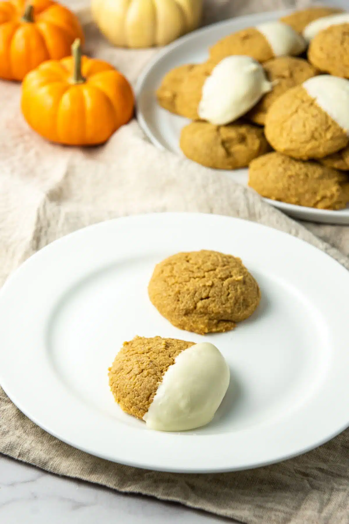 Close up of a plate of two pumpkin cookies, one plain and one dipped in white chocolate