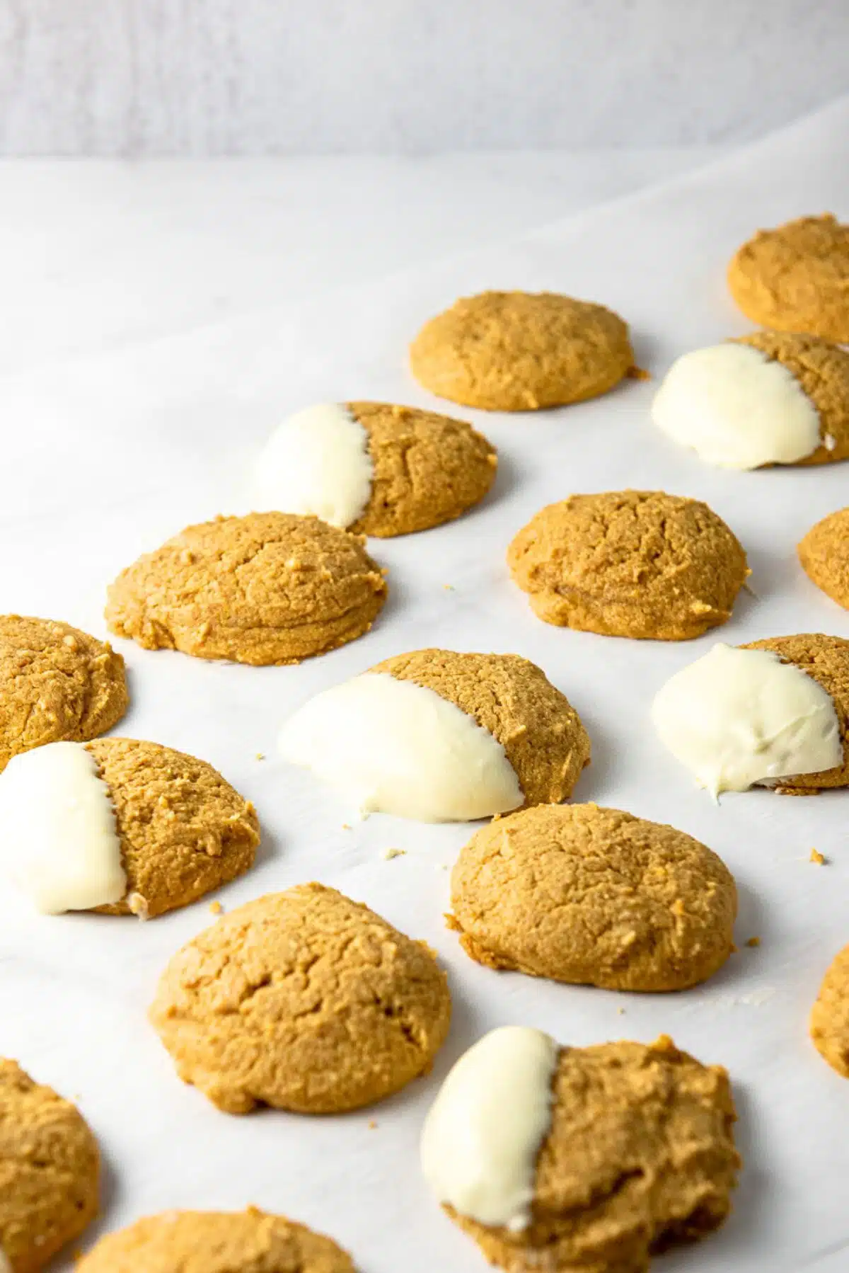 Parchment paper filled with pumpkin cookies, some dipped in white chocolate