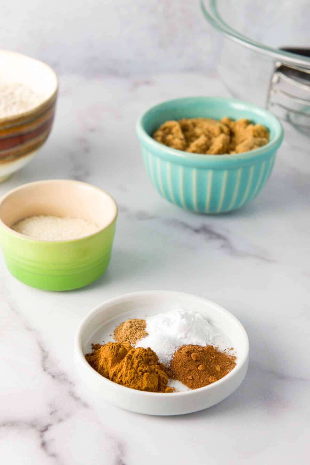 Spices, sugars and flour and a glass bowl in the background