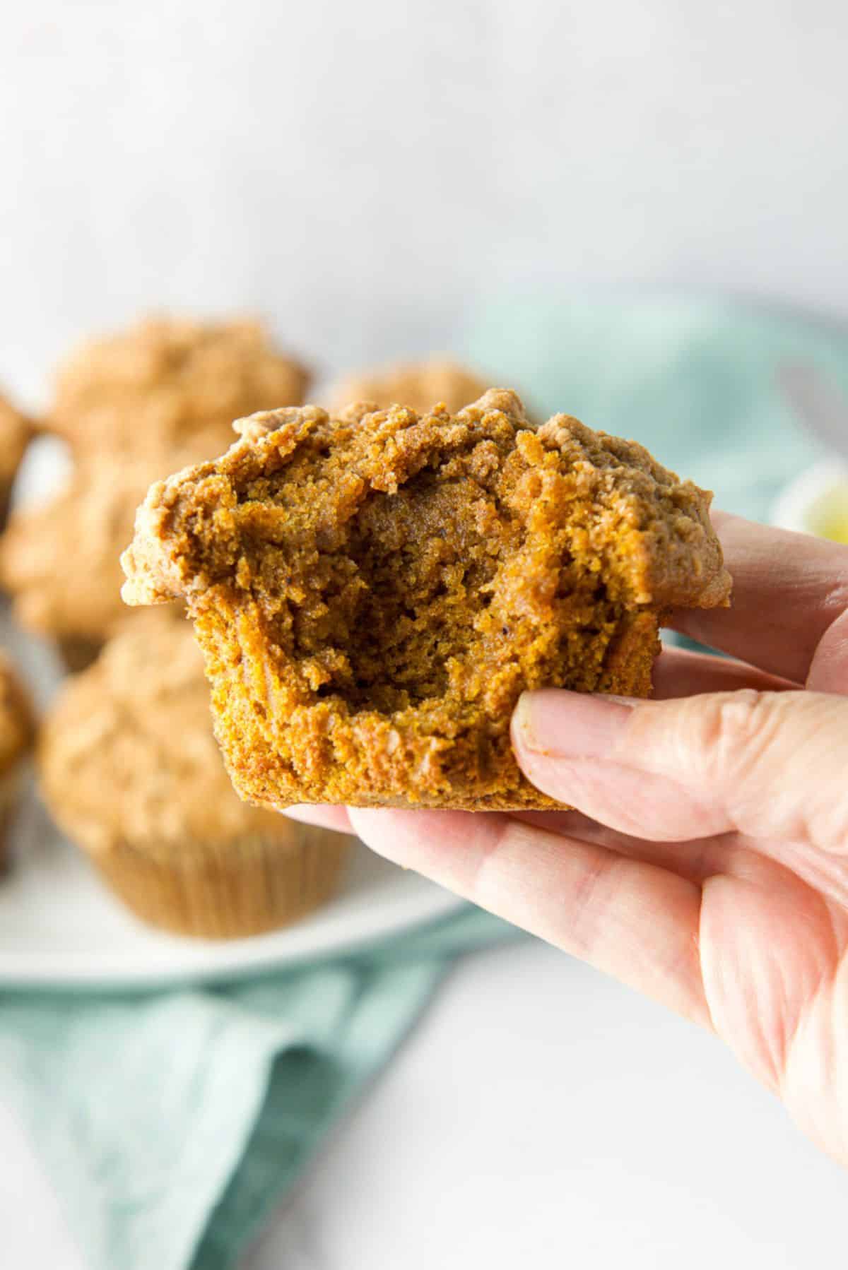 A hand holding a muffin with a bite taken out of it