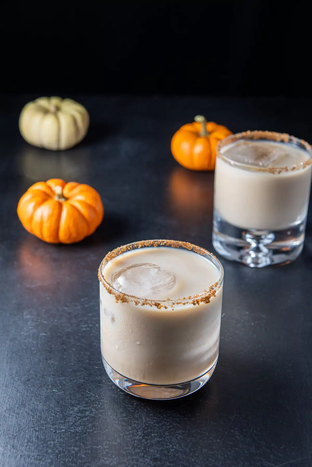 Creamy white Russian in the wider glass in front of the bubble glass with small pumpkins
