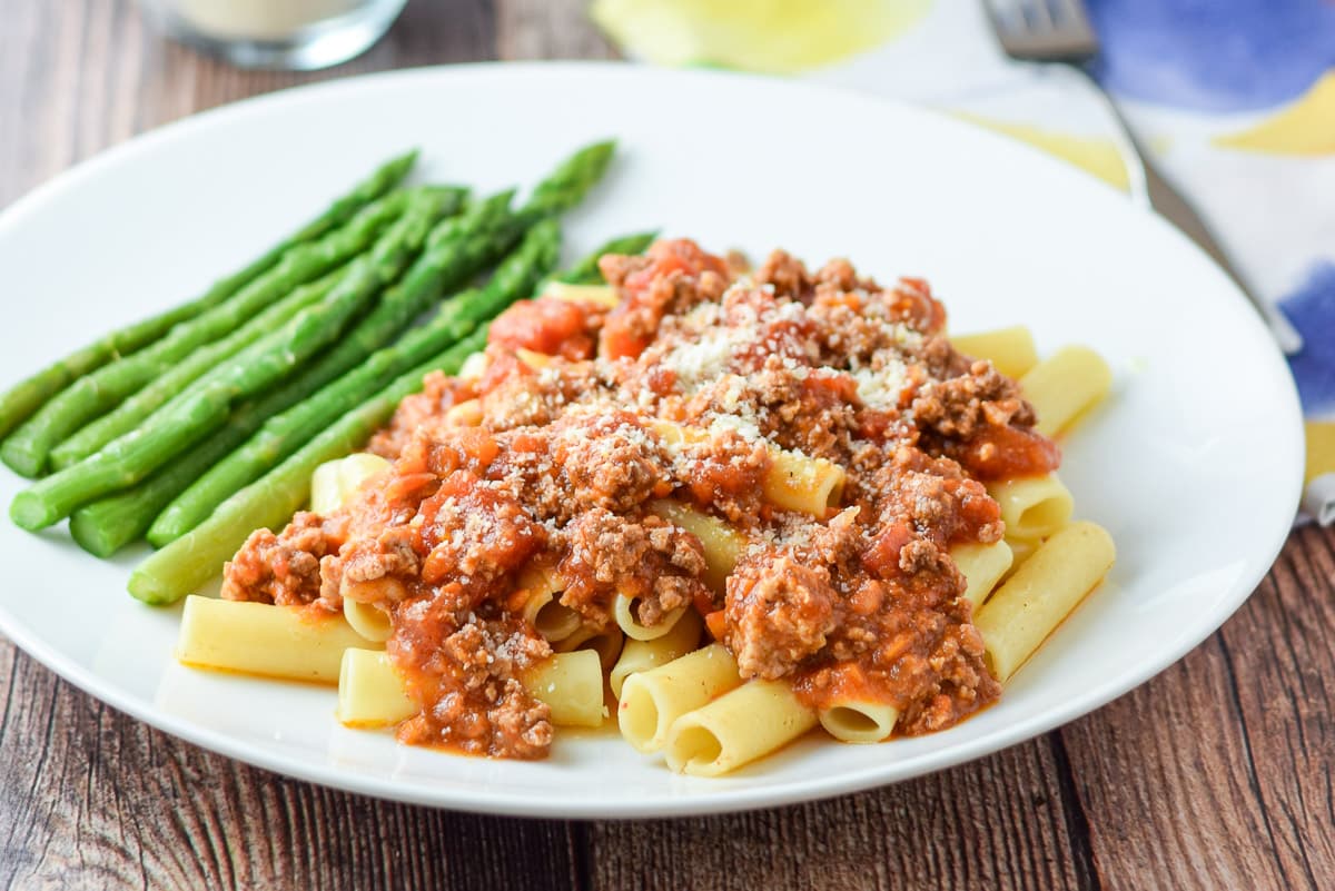 Parmesan cheese sprinkled on the gravy covered pasta with the pan of red sauce in the background