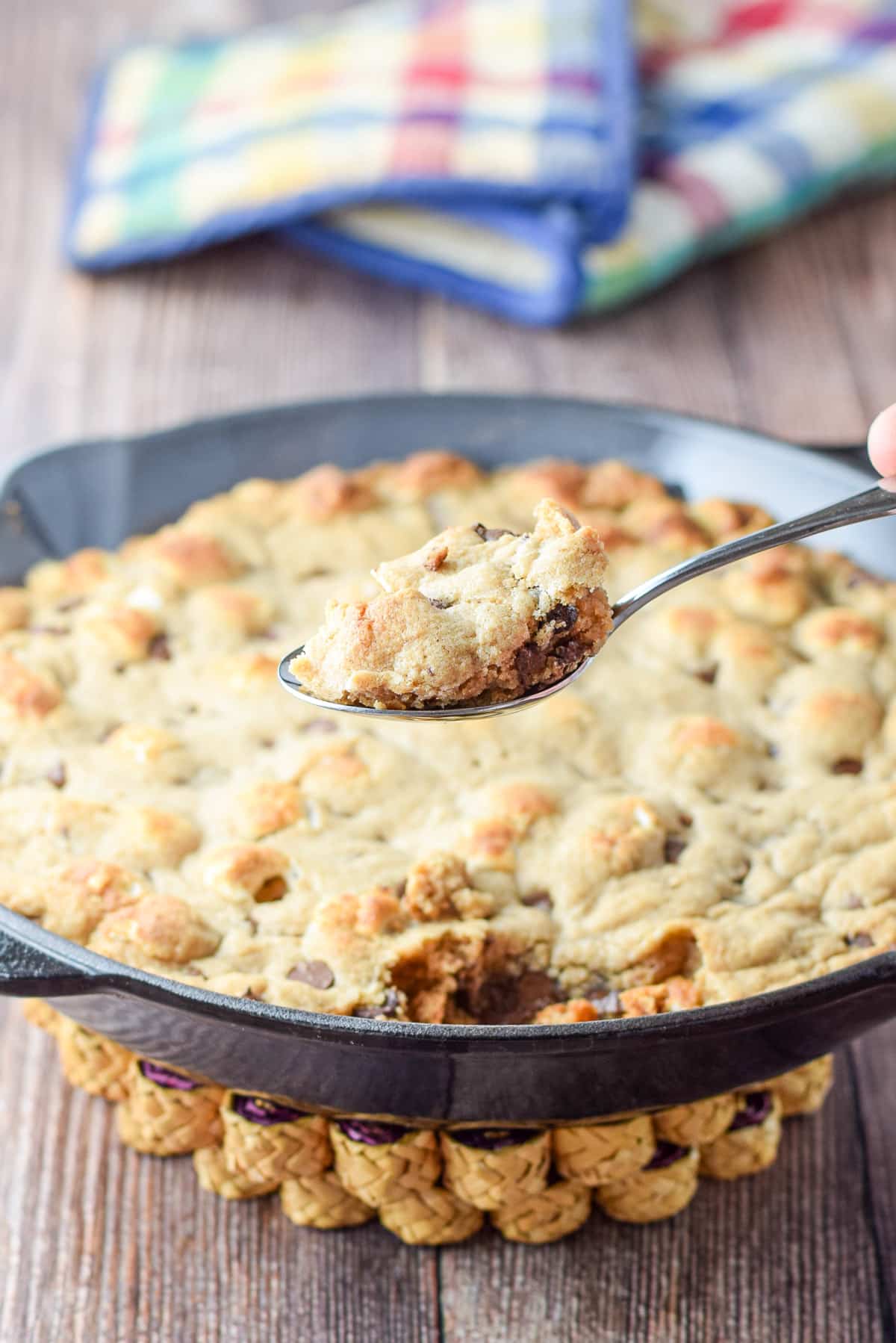 A hand holding a spoonful of cookie over the skillet