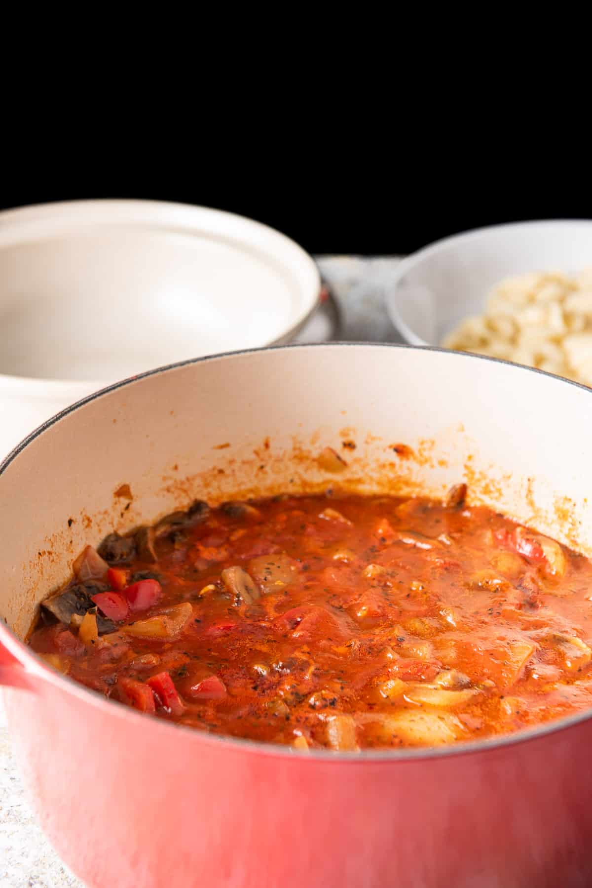 The gravy fully cooked but still in the pan. There is a beige bowl in the background and pasta in a dish
