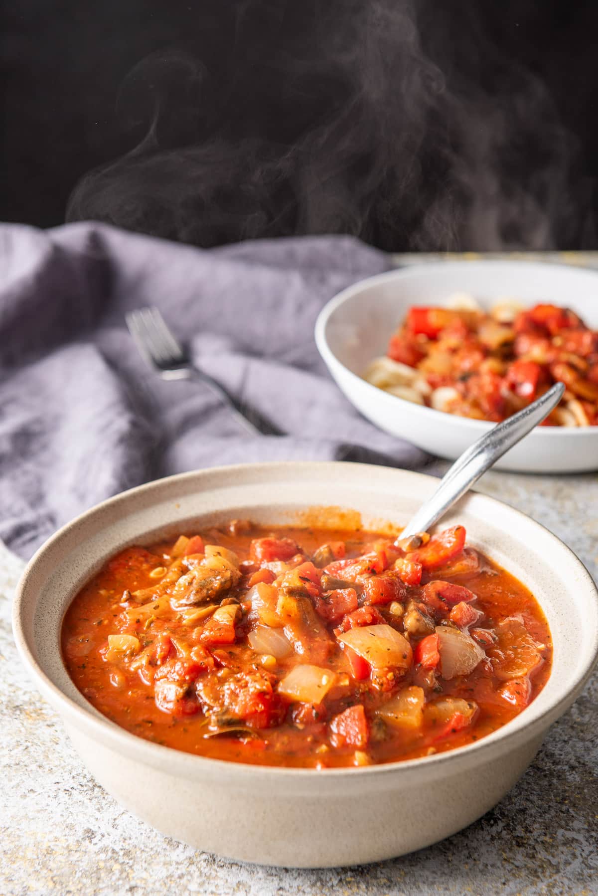 The tomato sauce in a beige bowl and a shallow bowl in the background with gravy on it