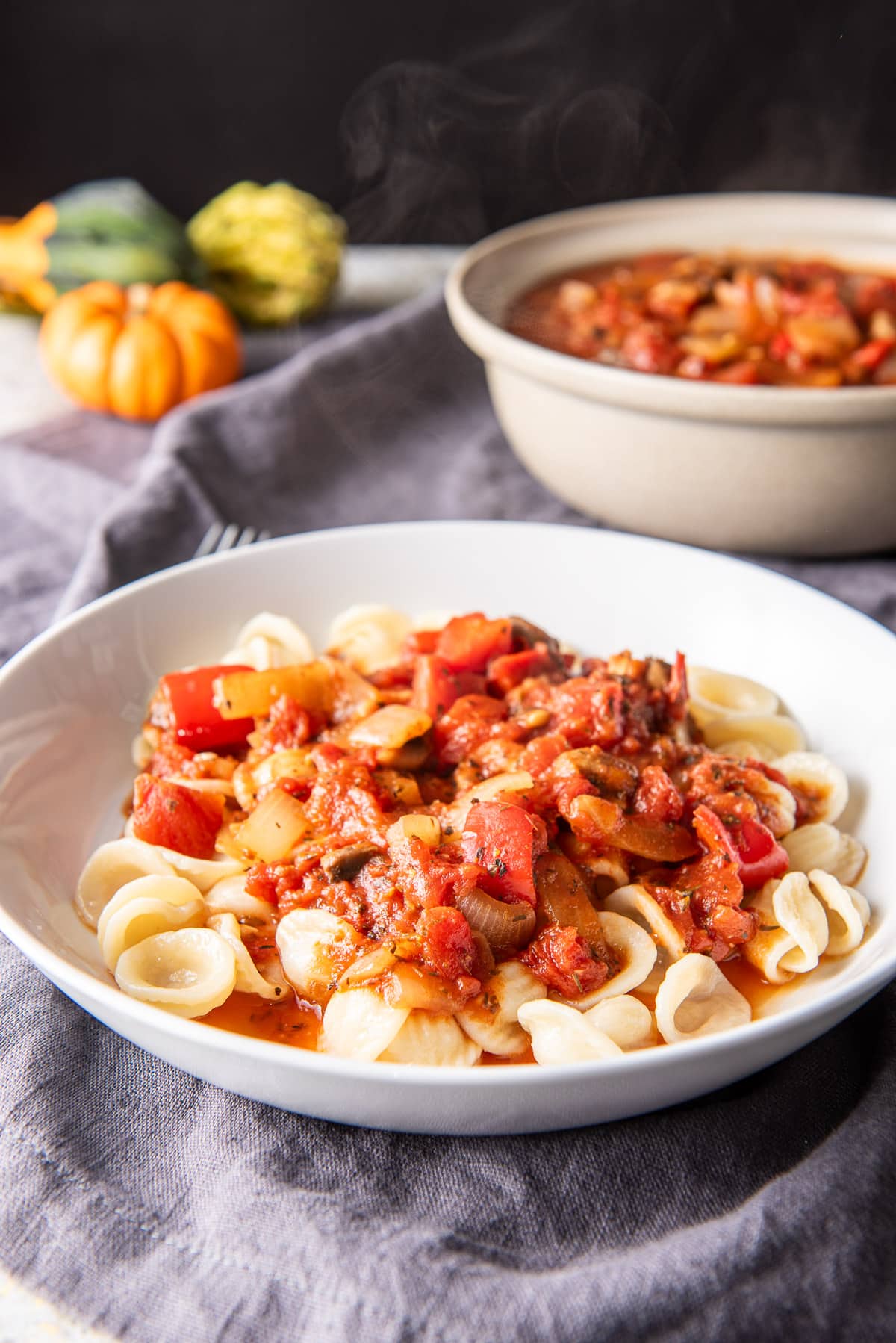 A white deep dish with pasta and red sauce on it with a bowl of the sauce in the back