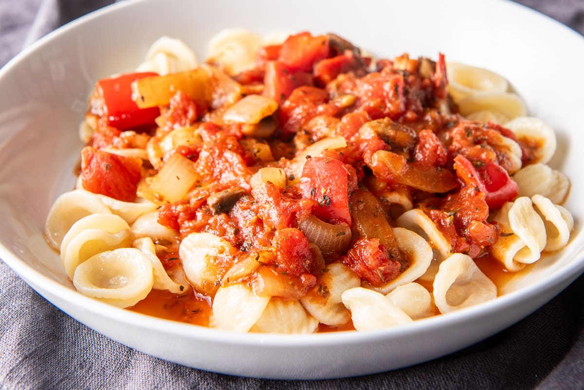 A shallow white bowl filled with pasta and gravy on a grey napkin