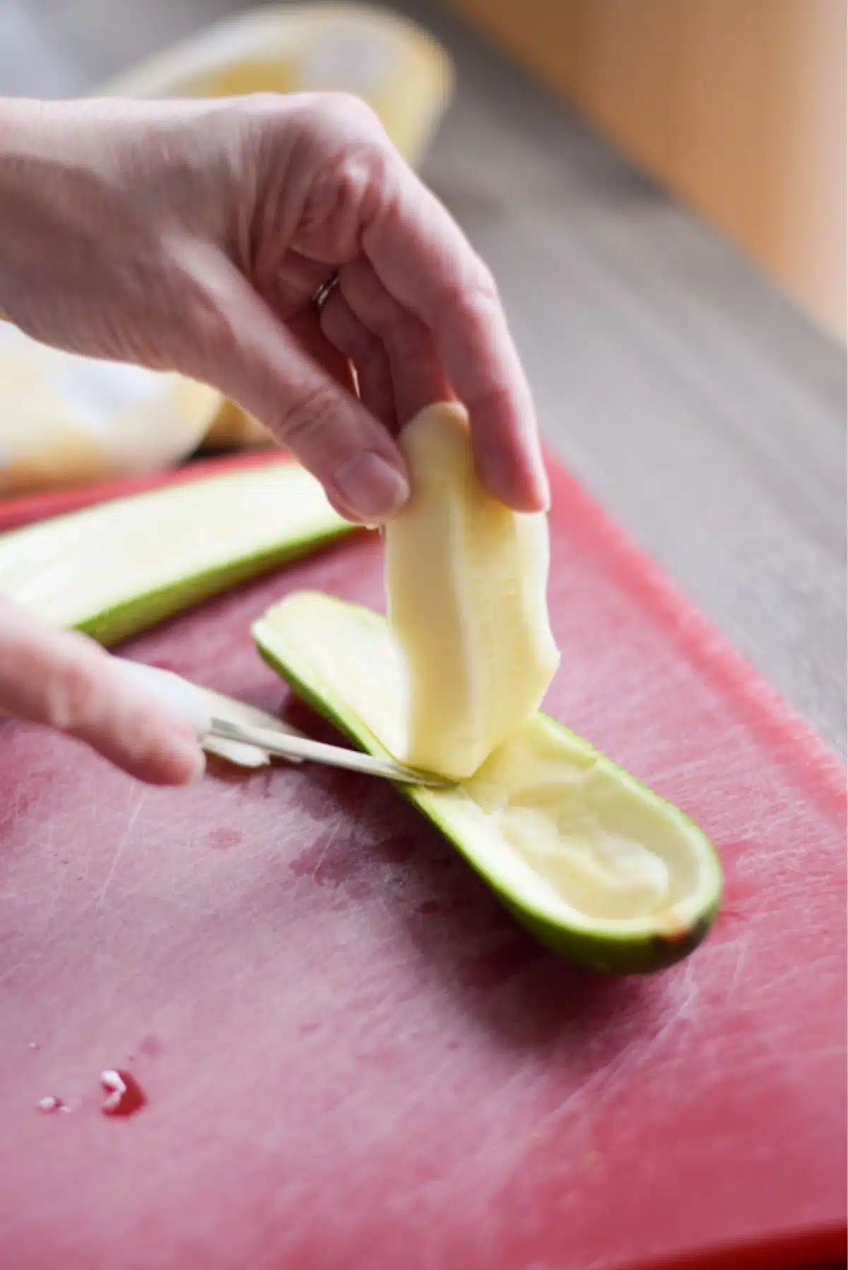 A woman's hand cutting into a zucchini cut lengthwise and removing the flesh