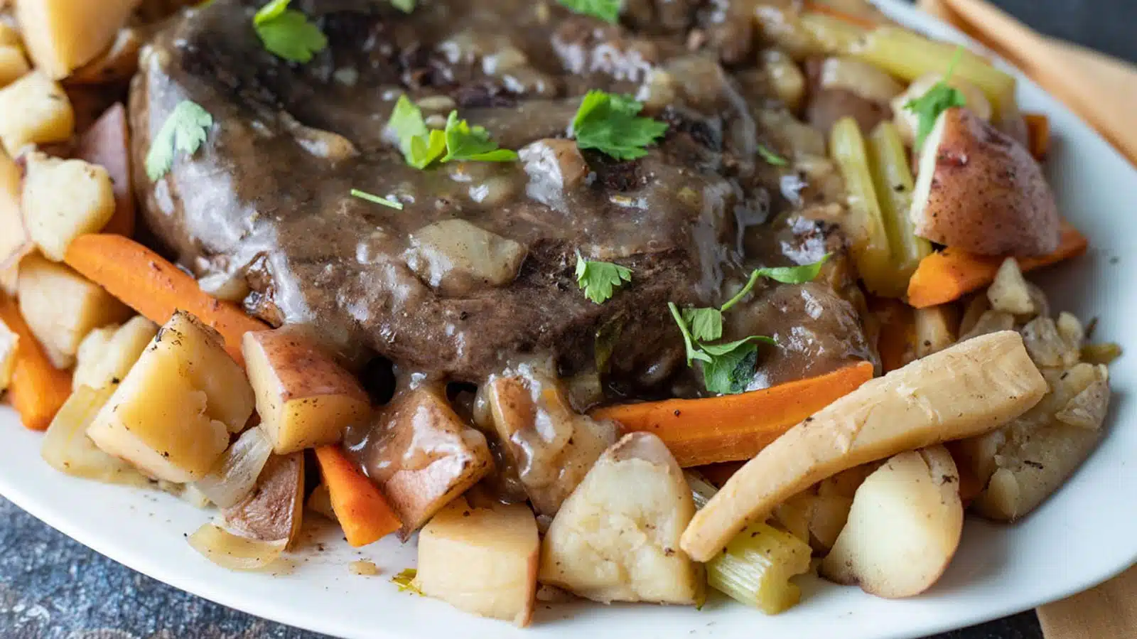 A white plate with vegetables and venison with gravy on top