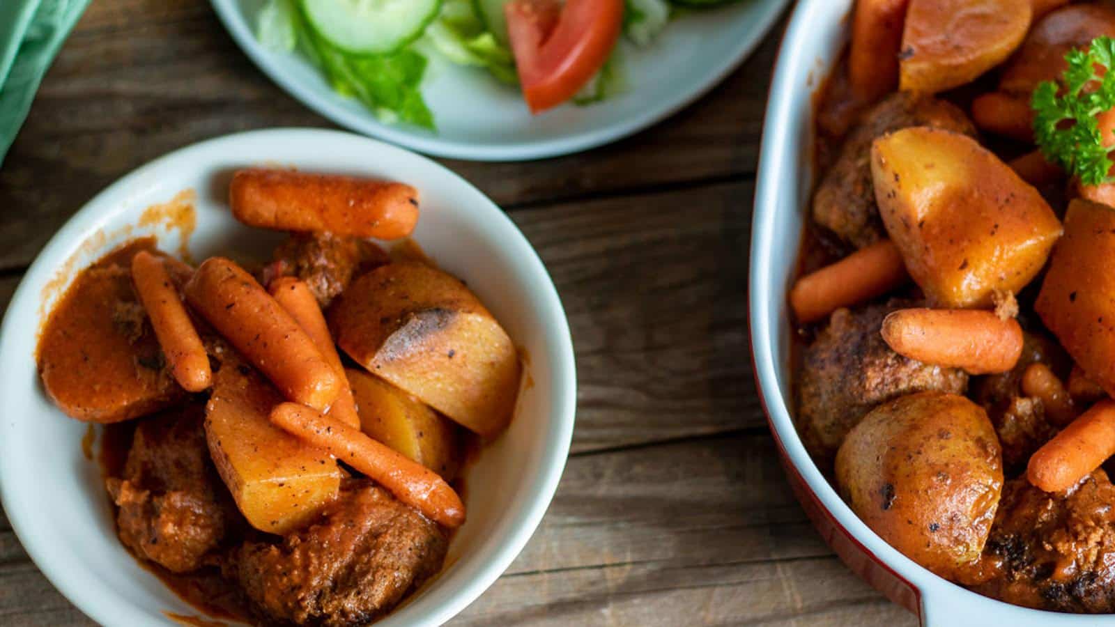 two white bowls with meatballs and vegetables with a salad in the shot as well