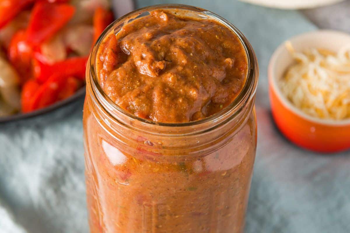 Near overhead view of the sauce in the jar, cheese, tortillas and vegetables