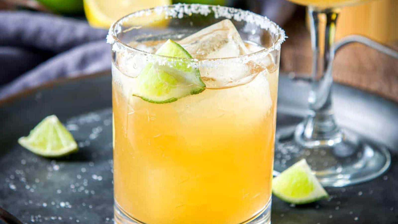 A salted glass with a margarita in it on a metal tray with lime wedges - square