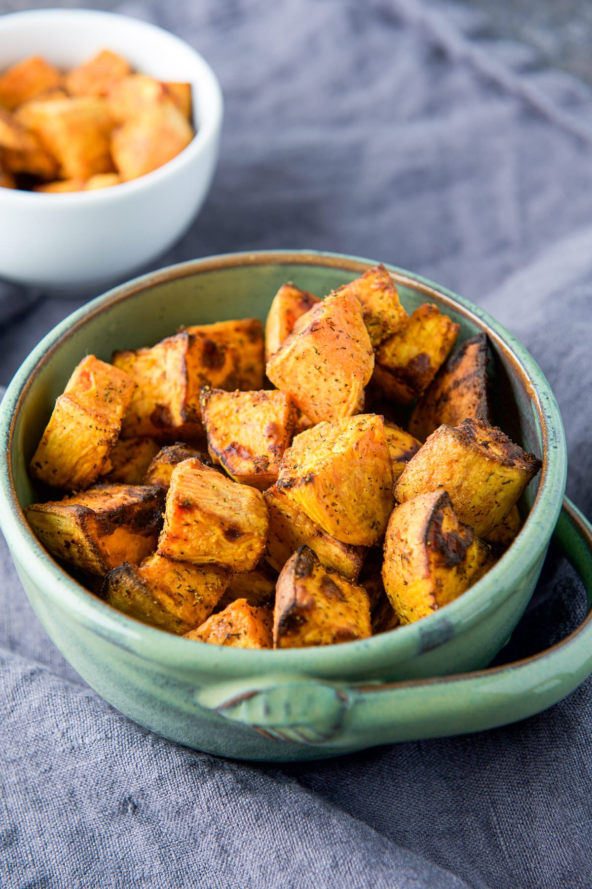 A green bowl with the cooked sweet potatoes in it along with a small white bowl in the back