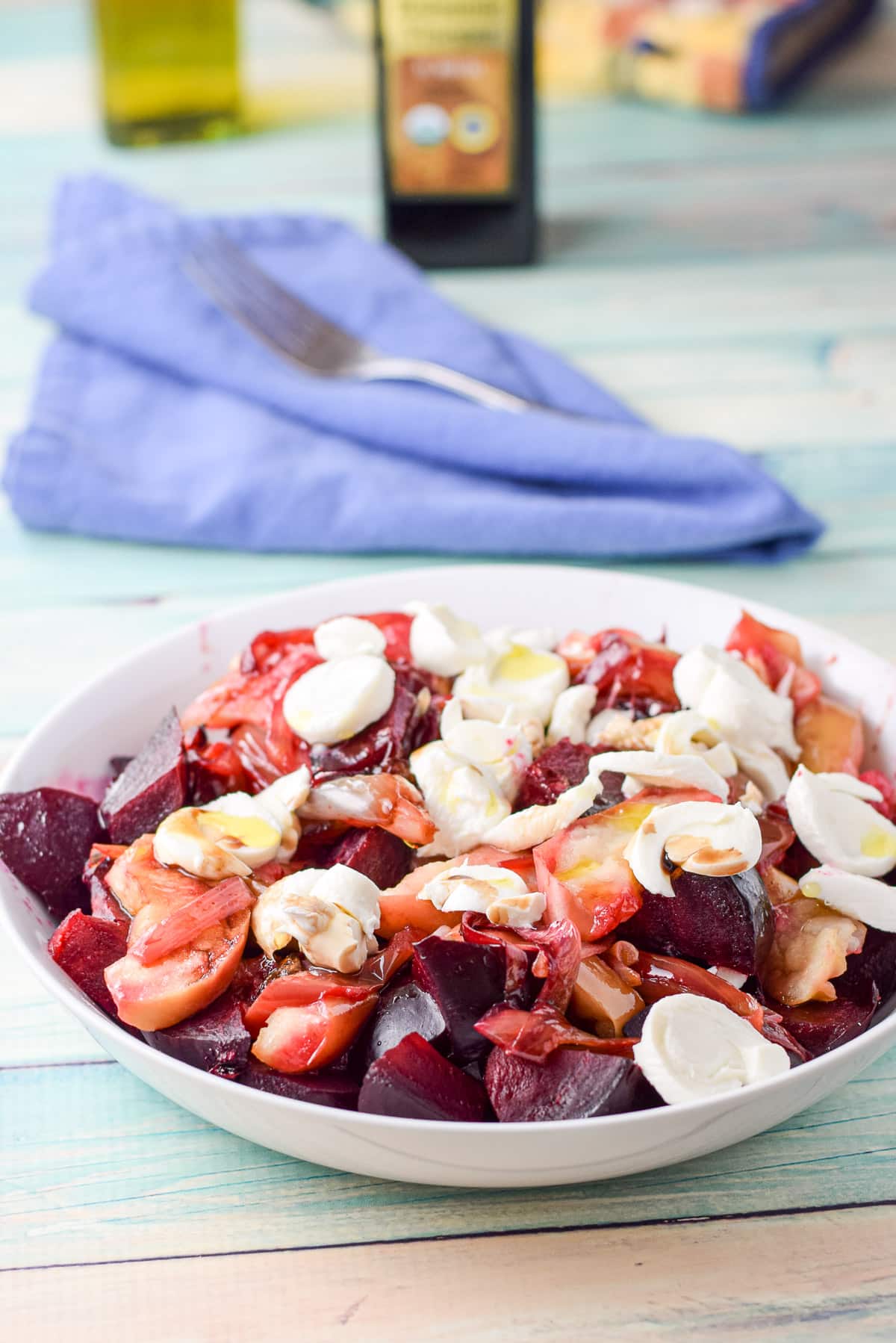 A deep dish with the beet and apple salad in it with olive oil and vinegar in the back
