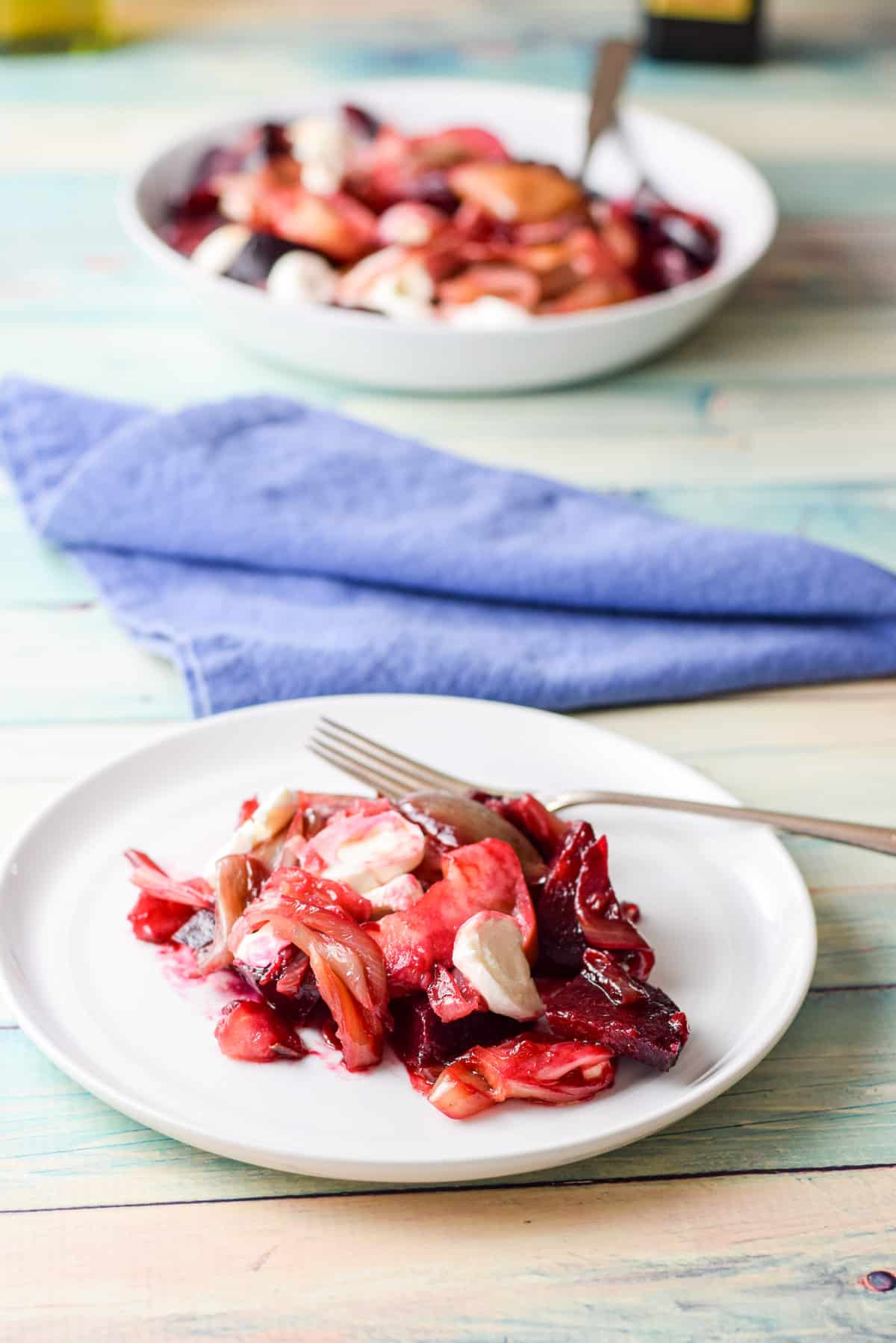 A small white plate with the apple beet salad and a fork, with the deep dish of it in the back