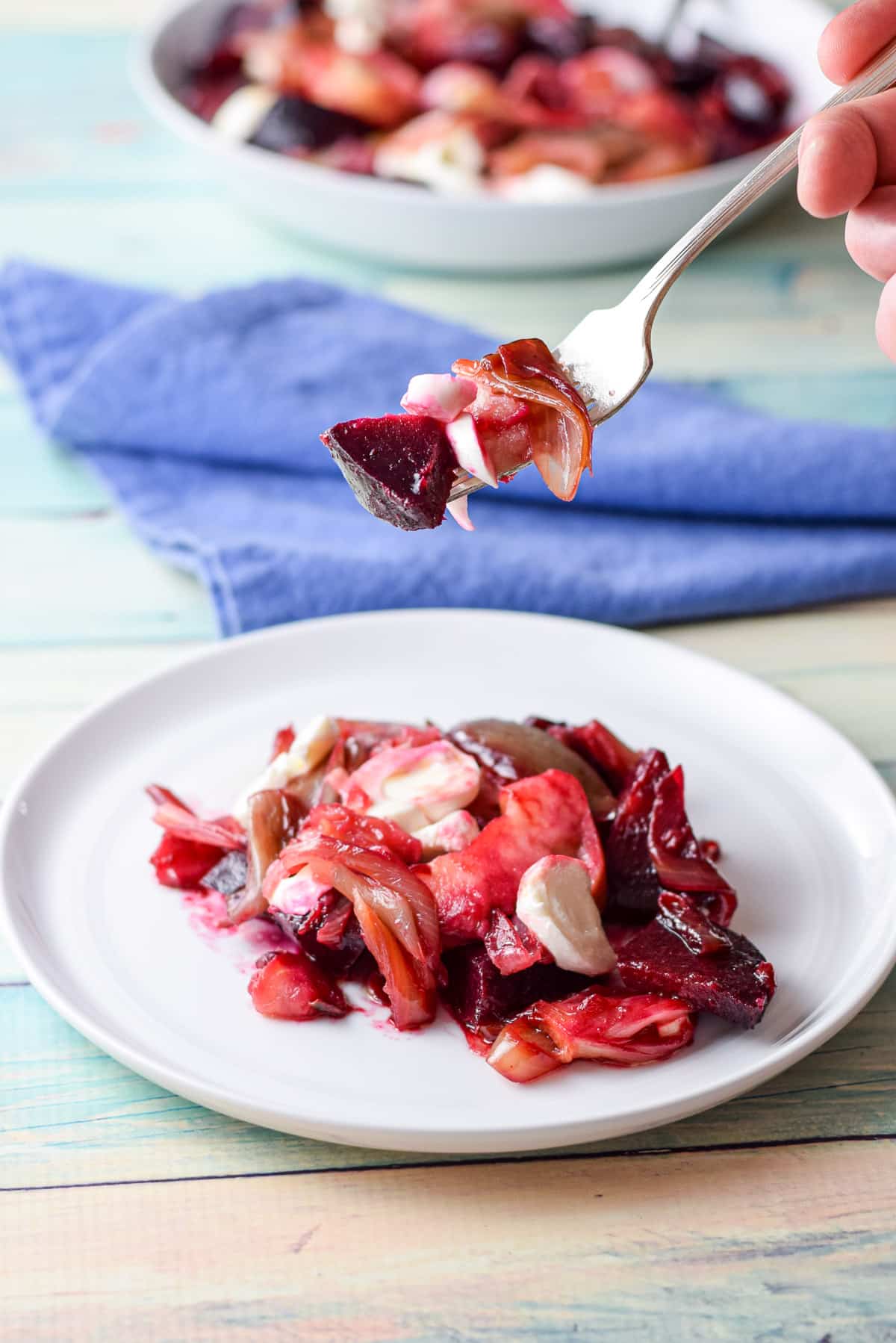 A fork with beets, apple, and cheese held over a white plate with the rest of the salad on it