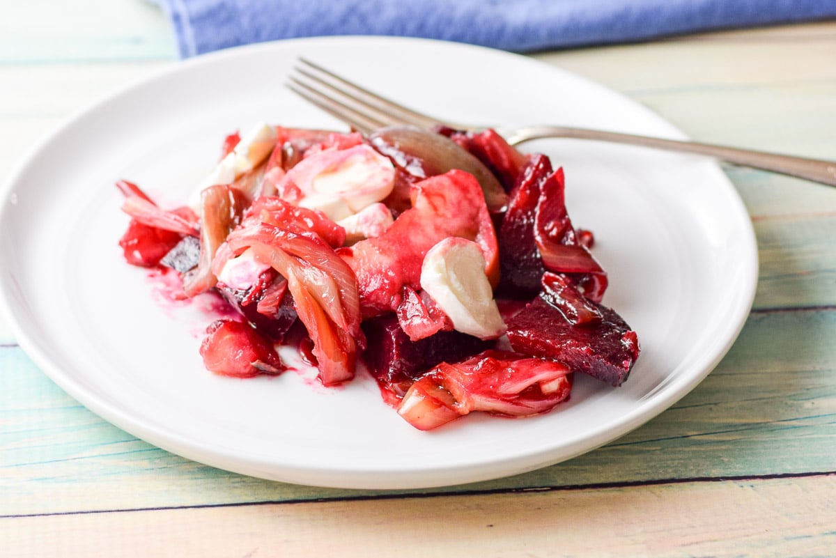 A white plate with onion, beet, apple, and cheese on it