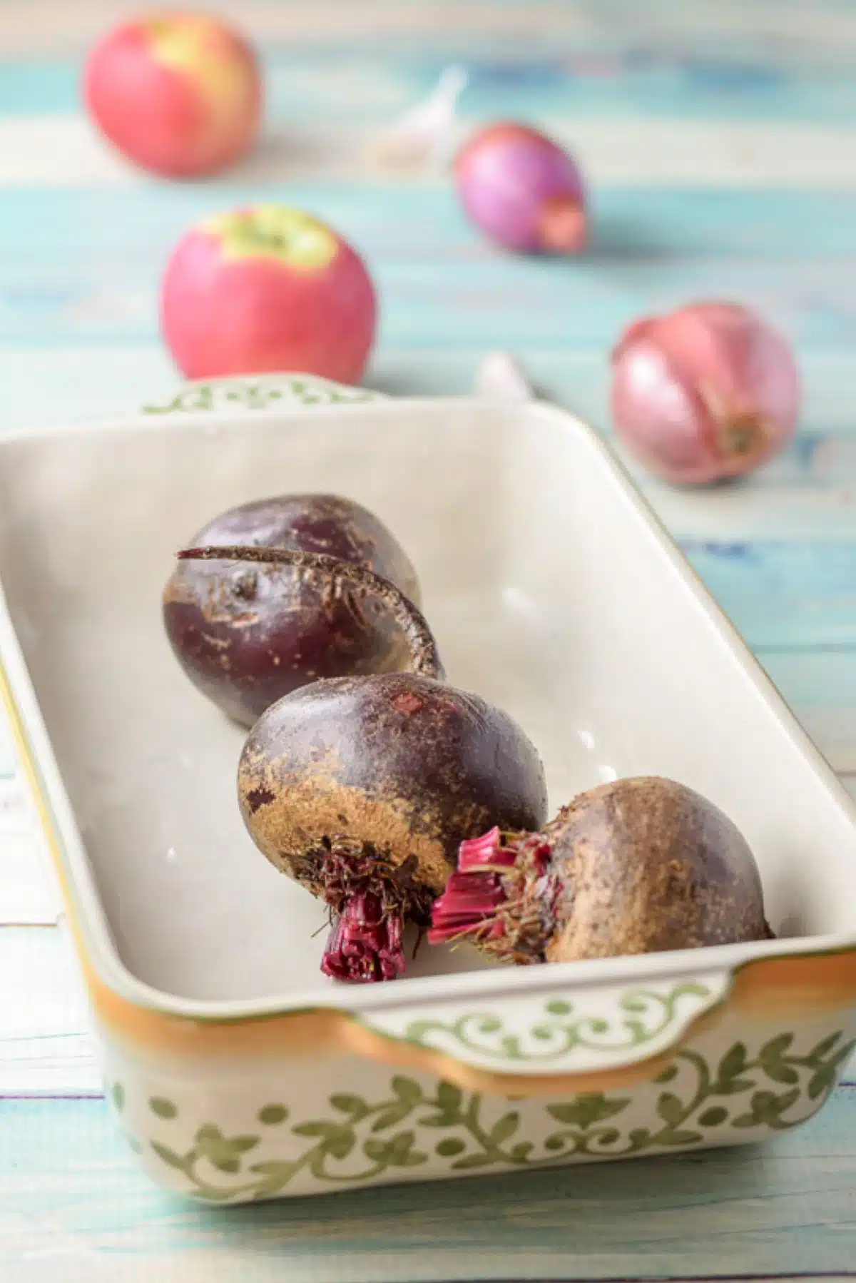 Beets in a baking dish with shallots and apples in the background