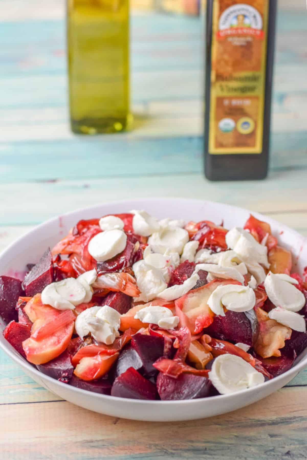 Mozzarella sliced on top of the salad with oil and balsamic vinegar in the background