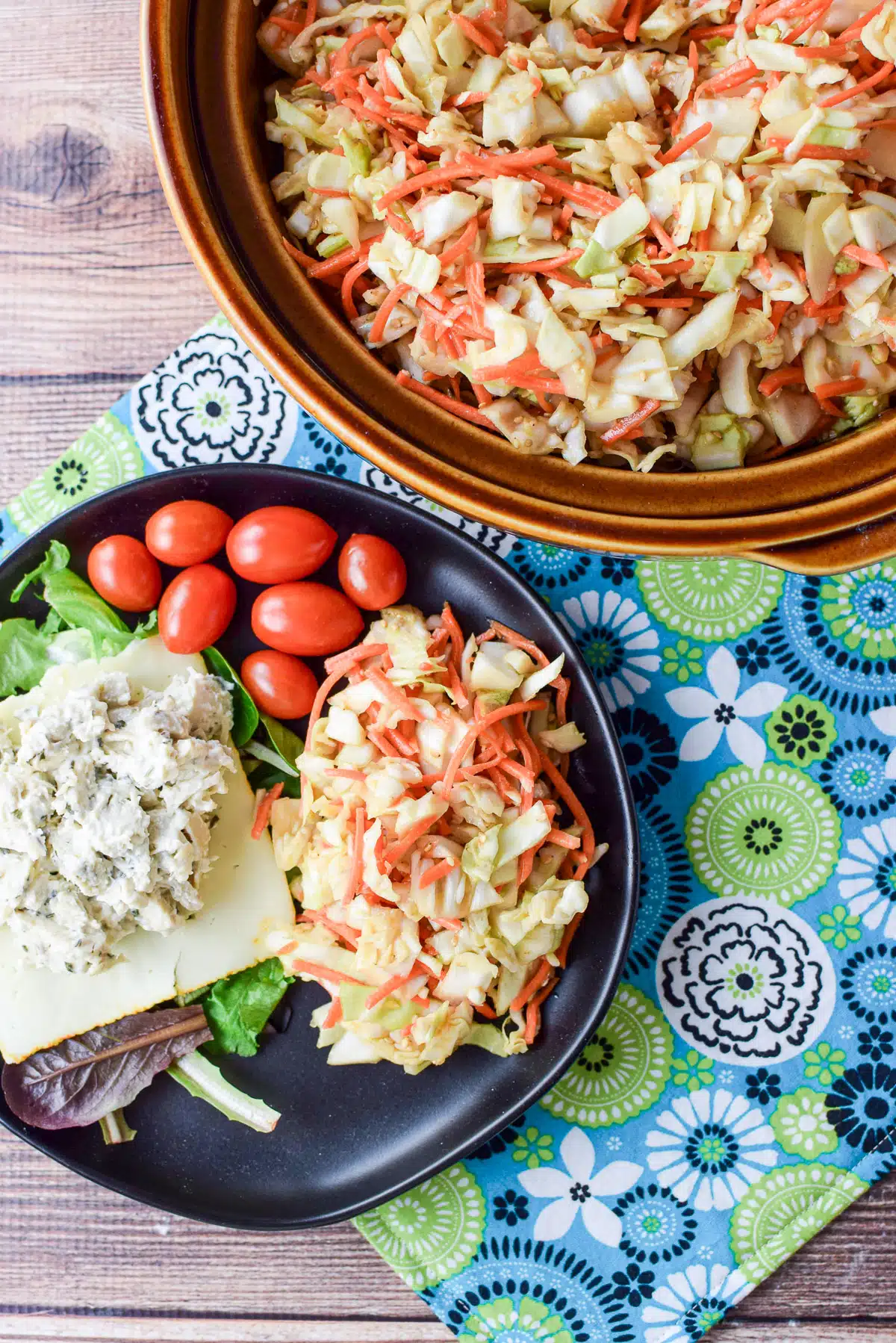 A black plate with slaw, tomatoes, lettuce and chicken salad