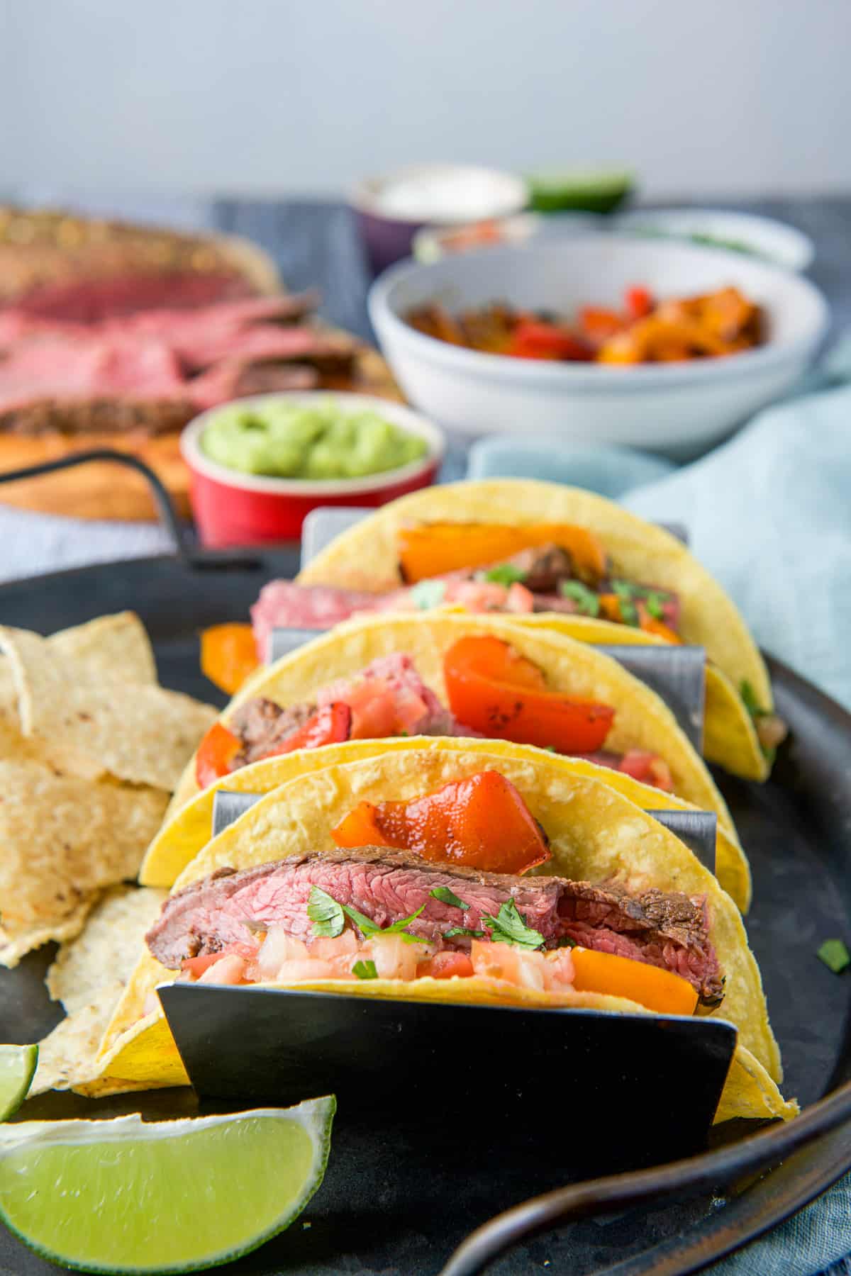 Three steak tacos, lime, and chips on a tray with the meat and garnishes for the tacos