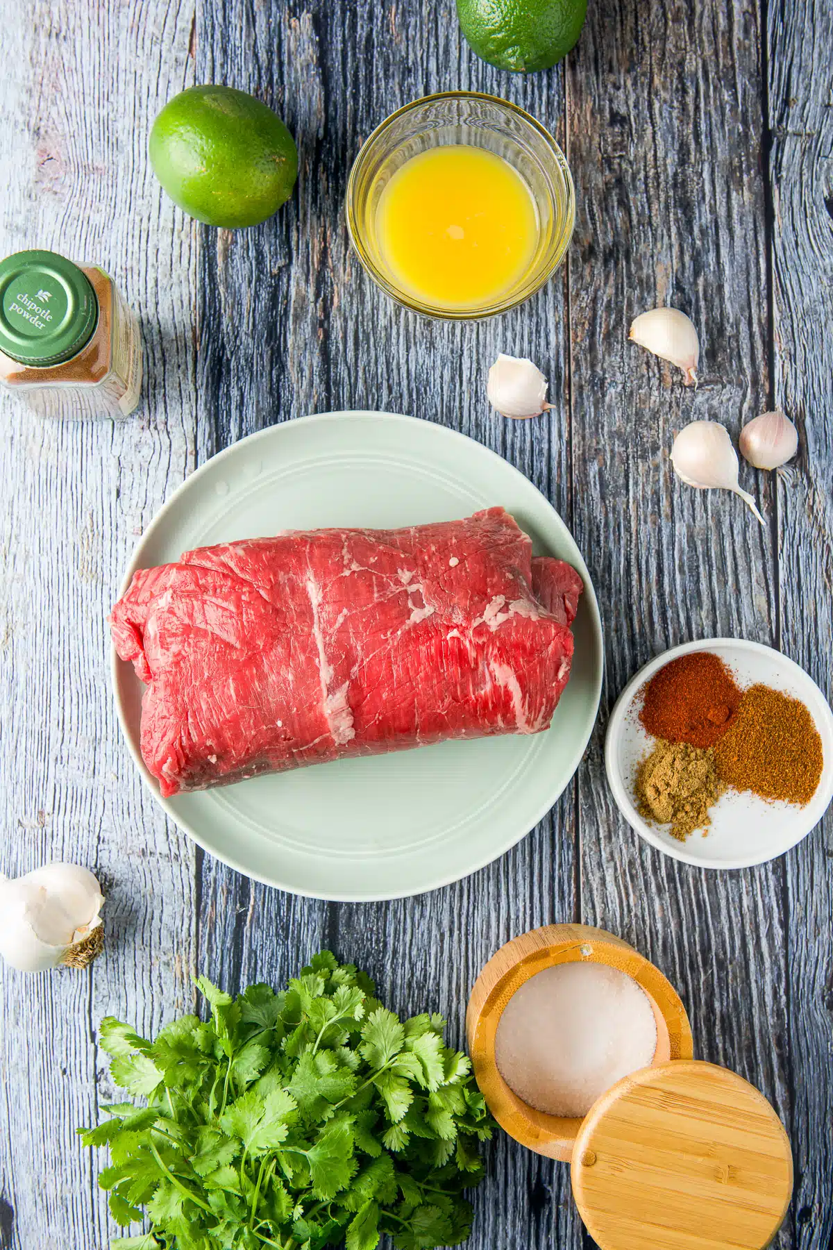Overhead view of ingredients for a steak taco - steak, cilantro, lime, orange juice, garlic, and salt