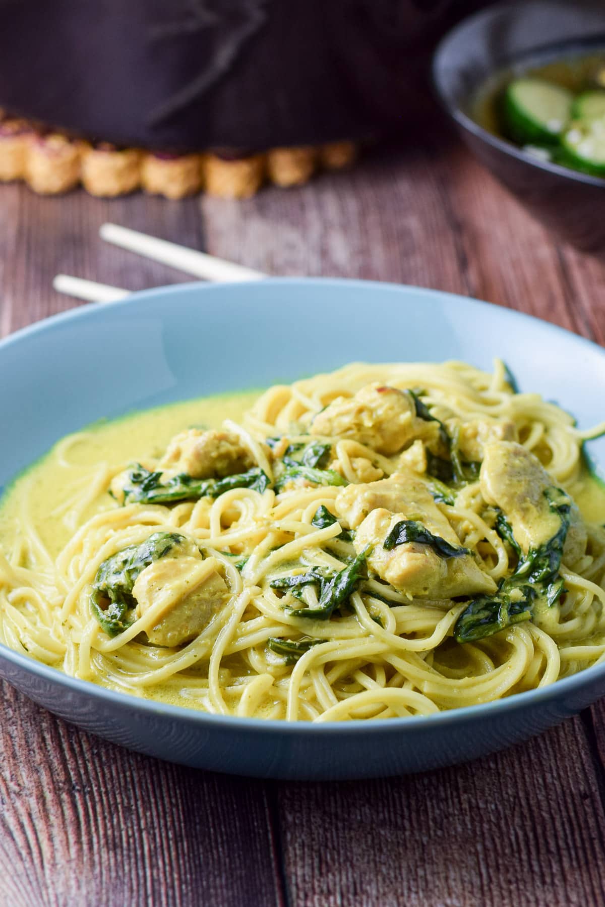 A blue deep dish with noodles, spinach, chicken, and curry sauce