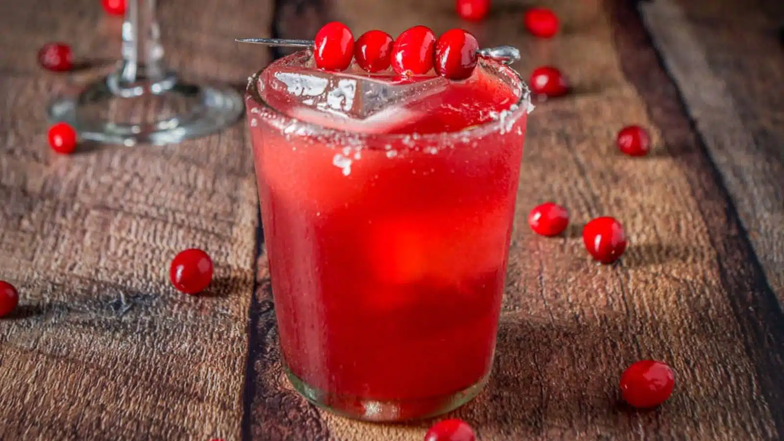 A double old fashioned glass filled with the cranberry drink with cranberries on the table and as garnish