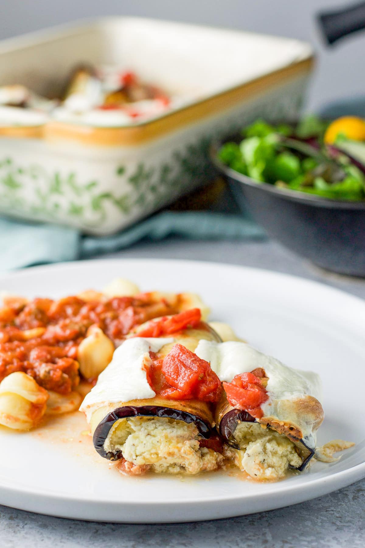 a white plate with stuffed rolled eggplant and pasta with sauce