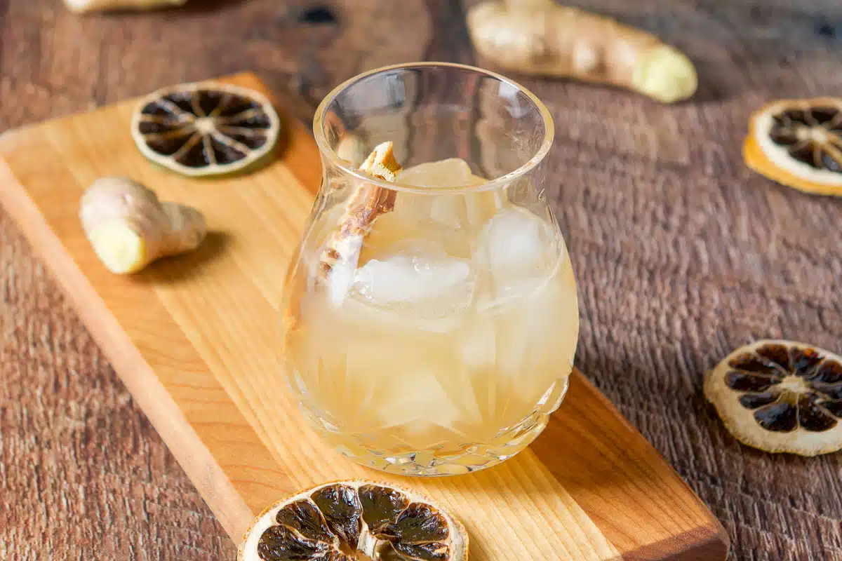 horizontal photo of a board with a amber drink on it with dried lemons and ginger