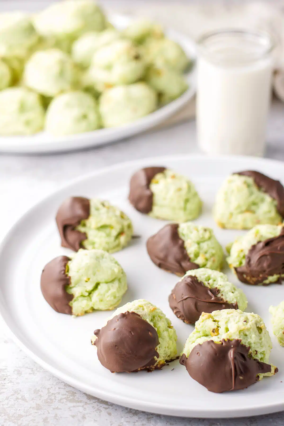 Close up of the chocolate dipped green cookies on a white plate with other the rest on a bigger plate in the background