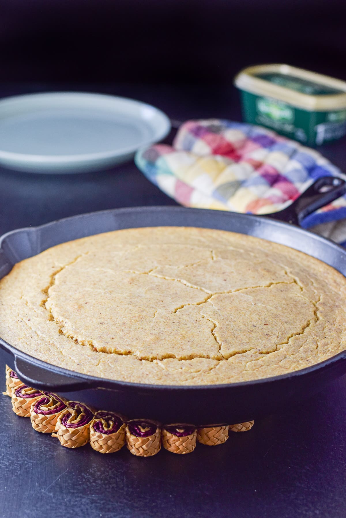 A cast iron pan with the cornbread baked and done. There is a plate and butter in the background