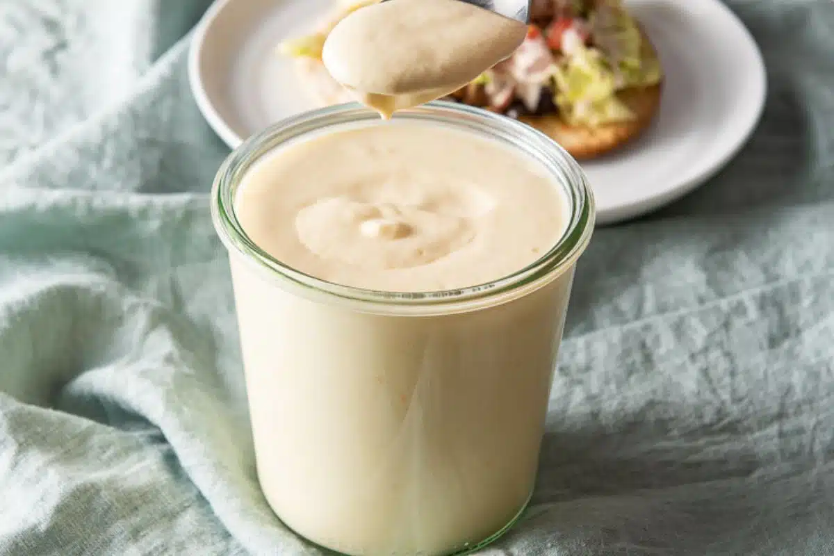 A jar with sour cream sauce in it with a spoon over the jar