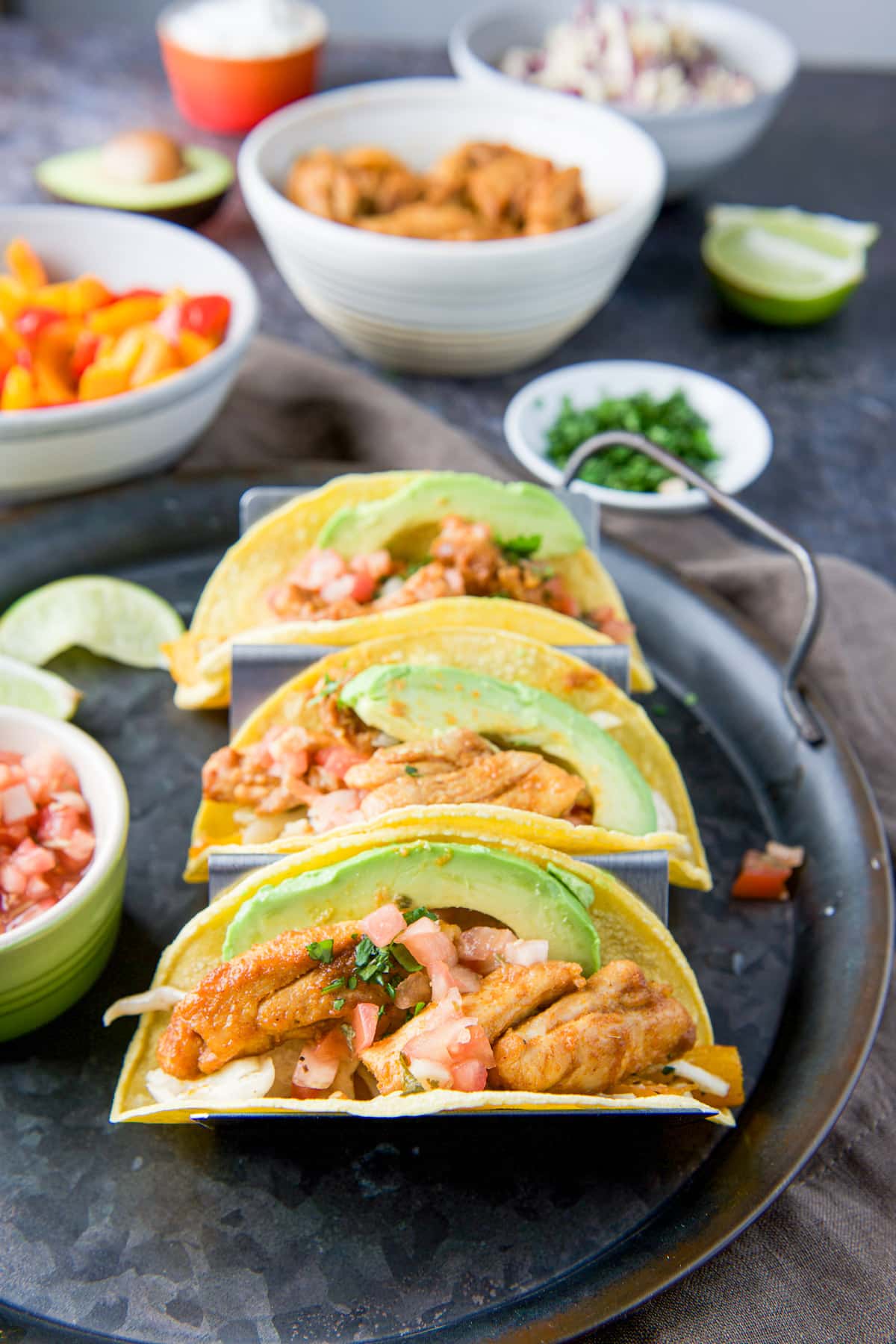 the tacos on a tray with bell peppers, avocado slices, chopped cilantro, and sour cream