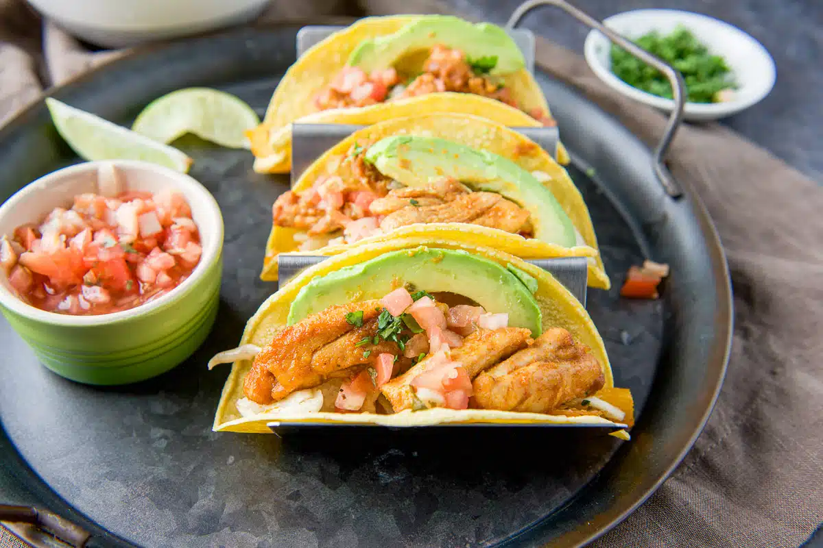 horizontal photo of the chicken tacos with avocado, salsa, limes and cilantro