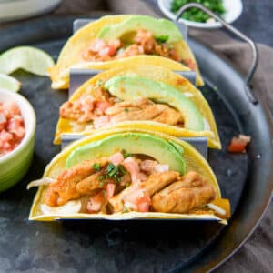 square photo of a metal plate with three tacos with chicken, avocado and pico de gallo