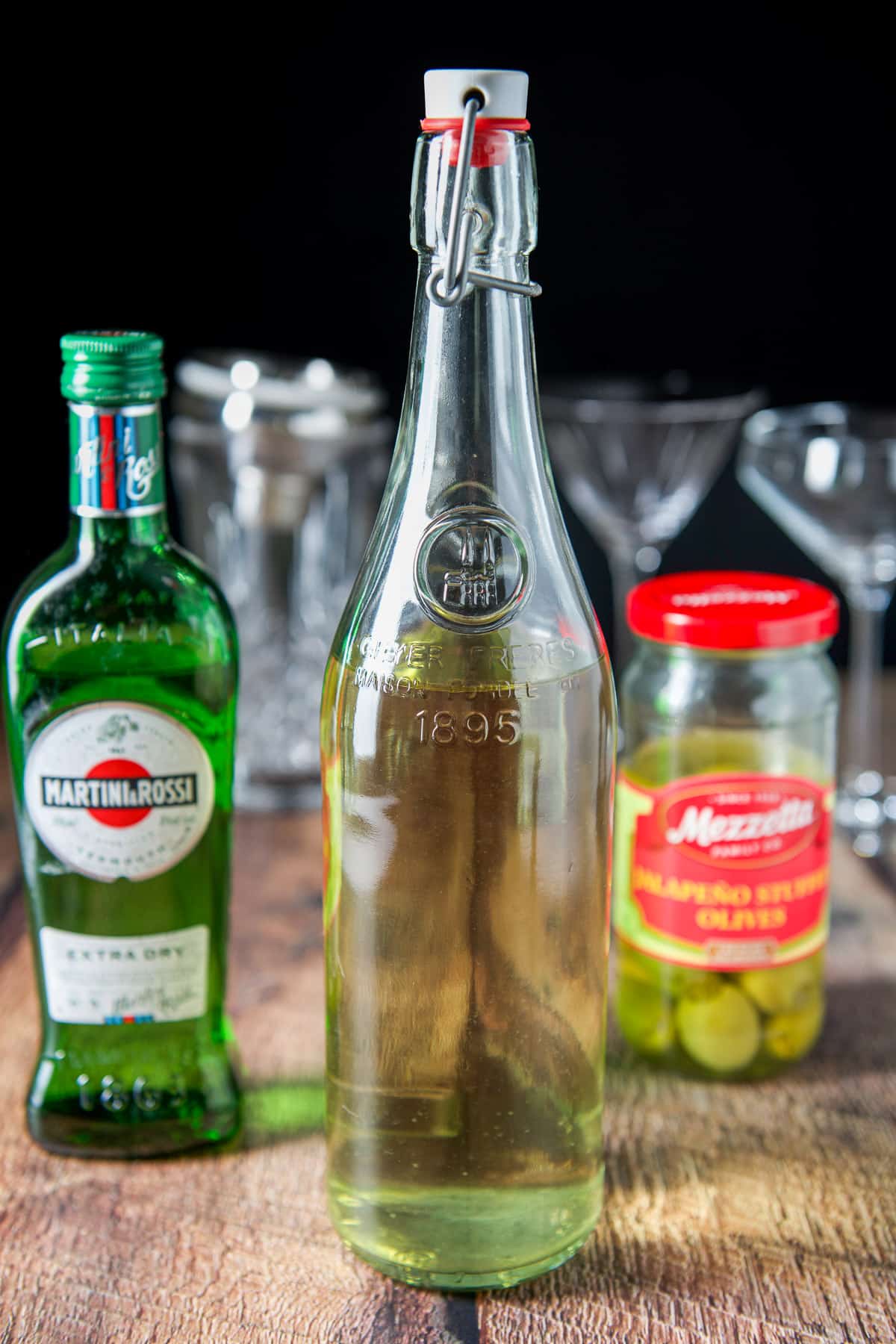Jalapeno vodka, dry vermouth, and olive brine on a table with glasses and a shaker