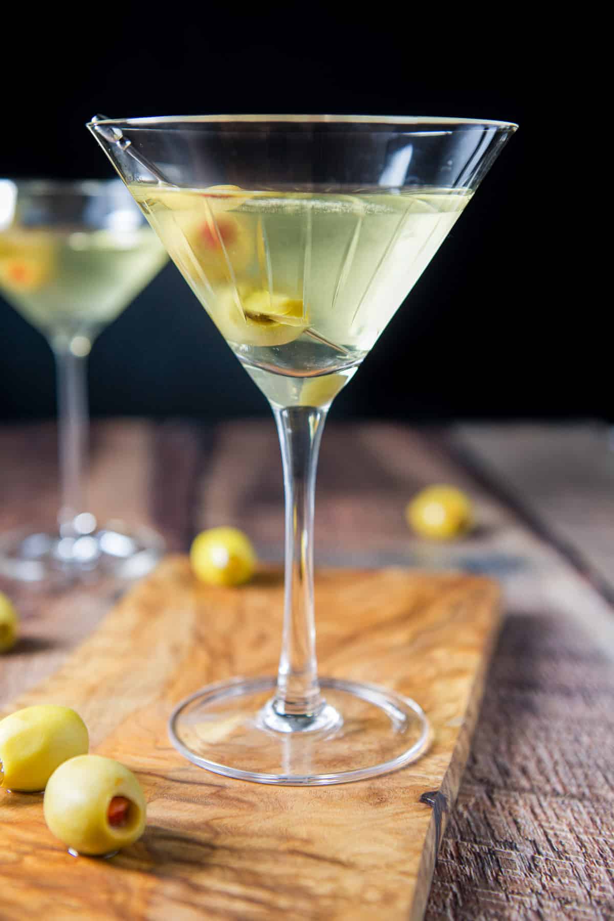 Vertical view of two martini glasses with olives as garnish and olives on the table
