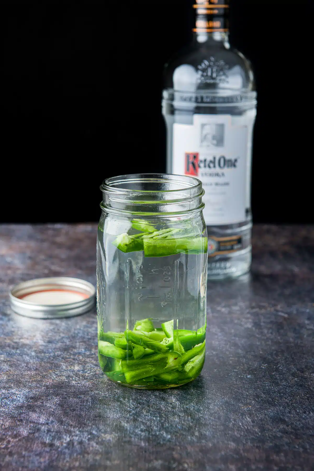 Vodka added to the jalapenos in the jar with the bottle of vodka in the background