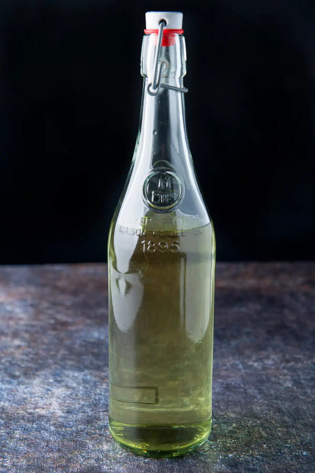 A tall glass bottle with a stopper filled with the green tinted vodka
