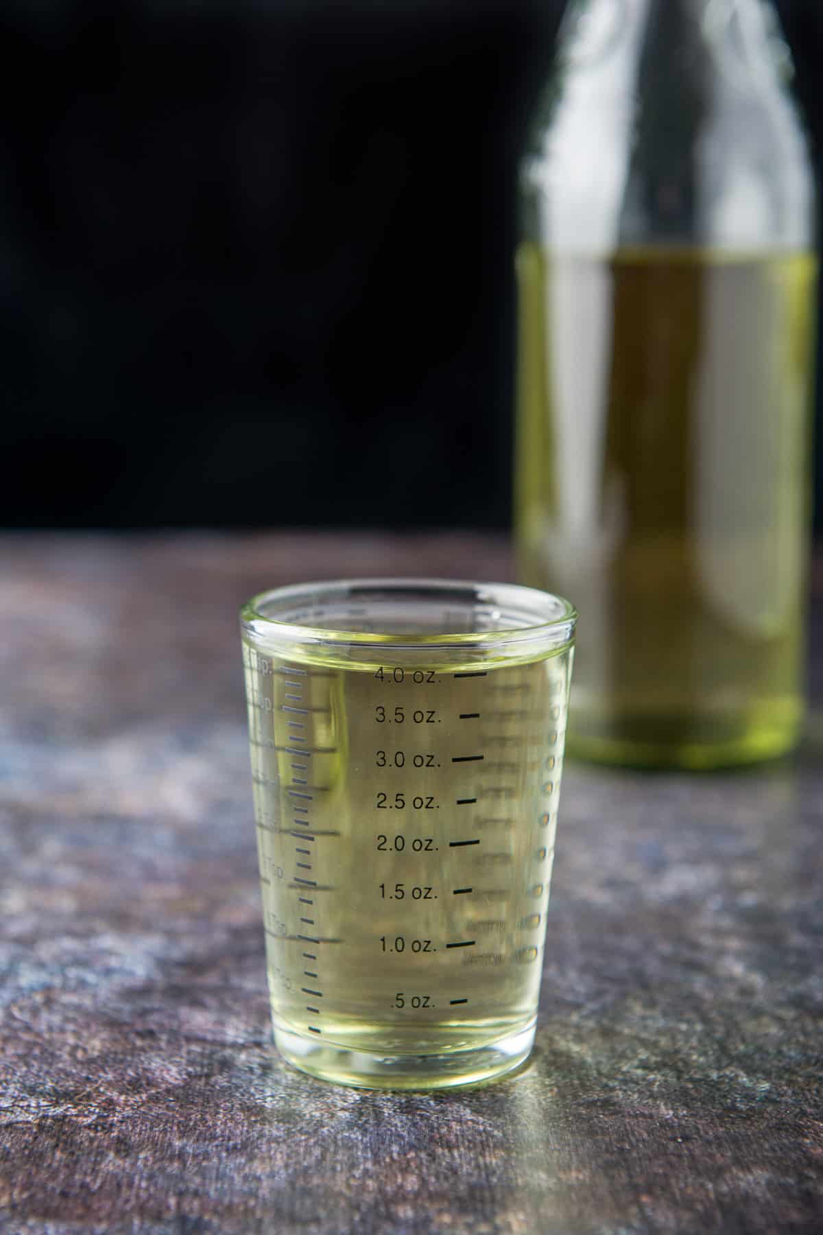 A shot glass with 4 ounces of jalapeno vodka with a large bottle filled with it in the back