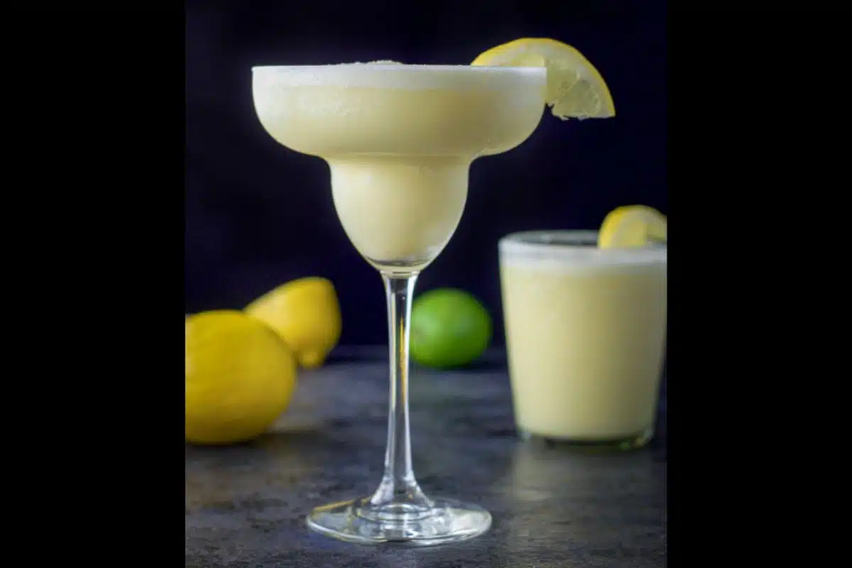 Two margarita glasses with the lemon margarita in them with lemon slices as garnish on the side of the glass