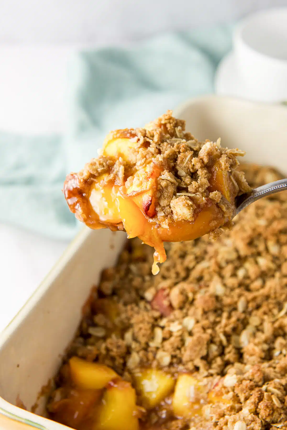 A big spoonful of peaches with crumble topping held over the baking dish